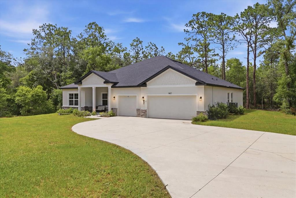A single-story house with a three-car garage and a covered front porch sits on a lawn — 1427 W MINERAL COURT, HERNANDO, FL