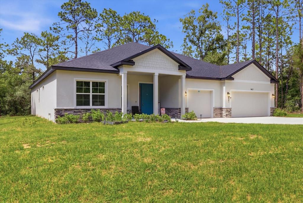 A single-story house with a blue front door, stone accents, and a two-car garage — 1427 W MINERAL COURT, HERNANDO, FL