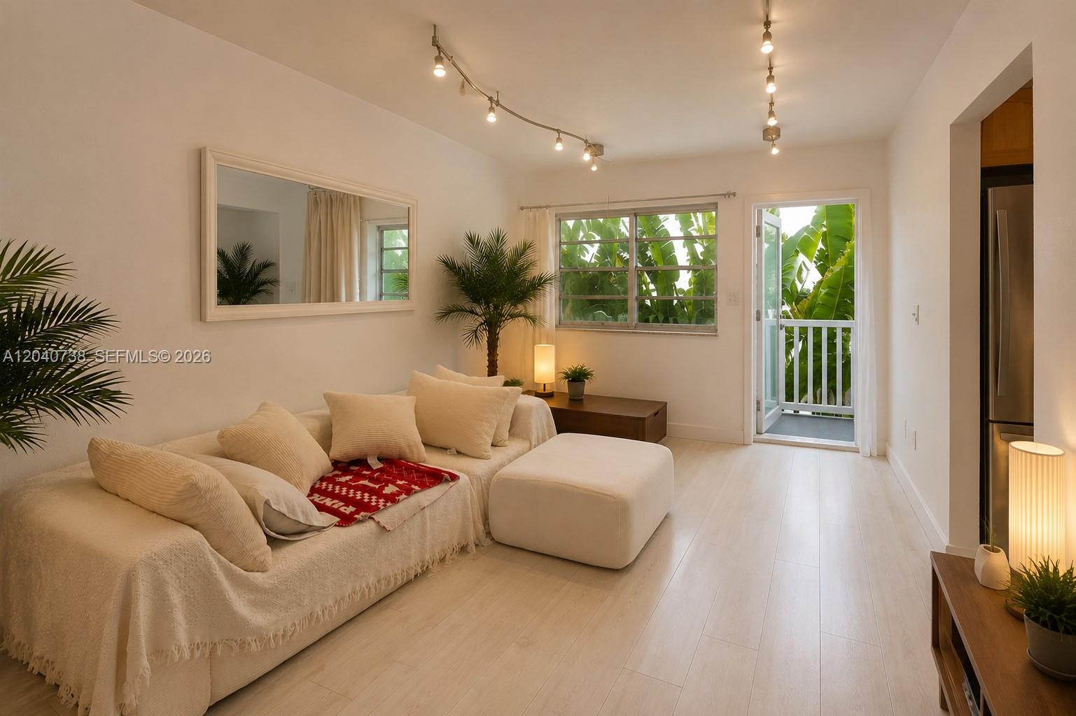 A living room features a white sofa, a mirror, track lighting, and a balcony door — 344 Meridian Ave # 2B, Miami Beach FL 33139, MIAMI BEACH, FL