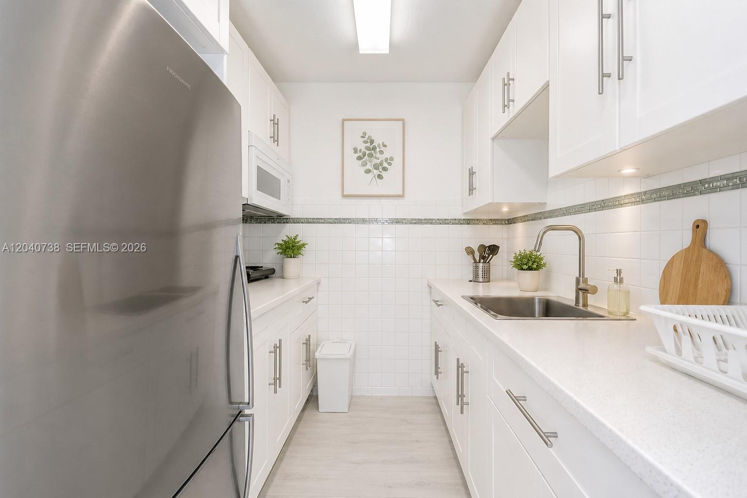 A galley kitchen features white cabinets, stainless steel appliances, and a white tiled backsplash — 344 Meridian Ave # 2B, Miami Beach FL 33139, MIAMI BEACH, FL