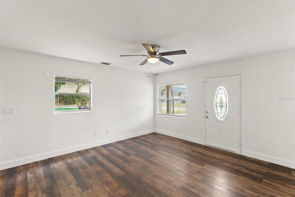 An empty room with white walls, dark wood-look flooring, a ceiling fan, and a front door — 1039 WOODLAND AVENUE, LAKELAND, FL