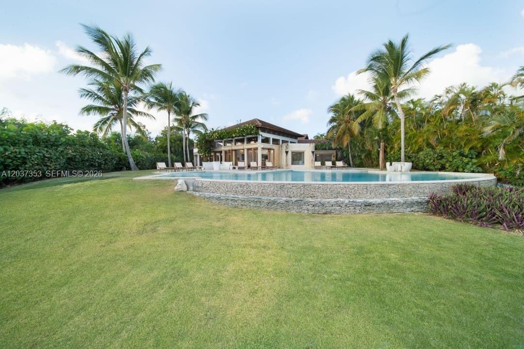 A large swimming pool sits in front of a modern house surrounded by palm trees — 0 Las palmas, FL, FL