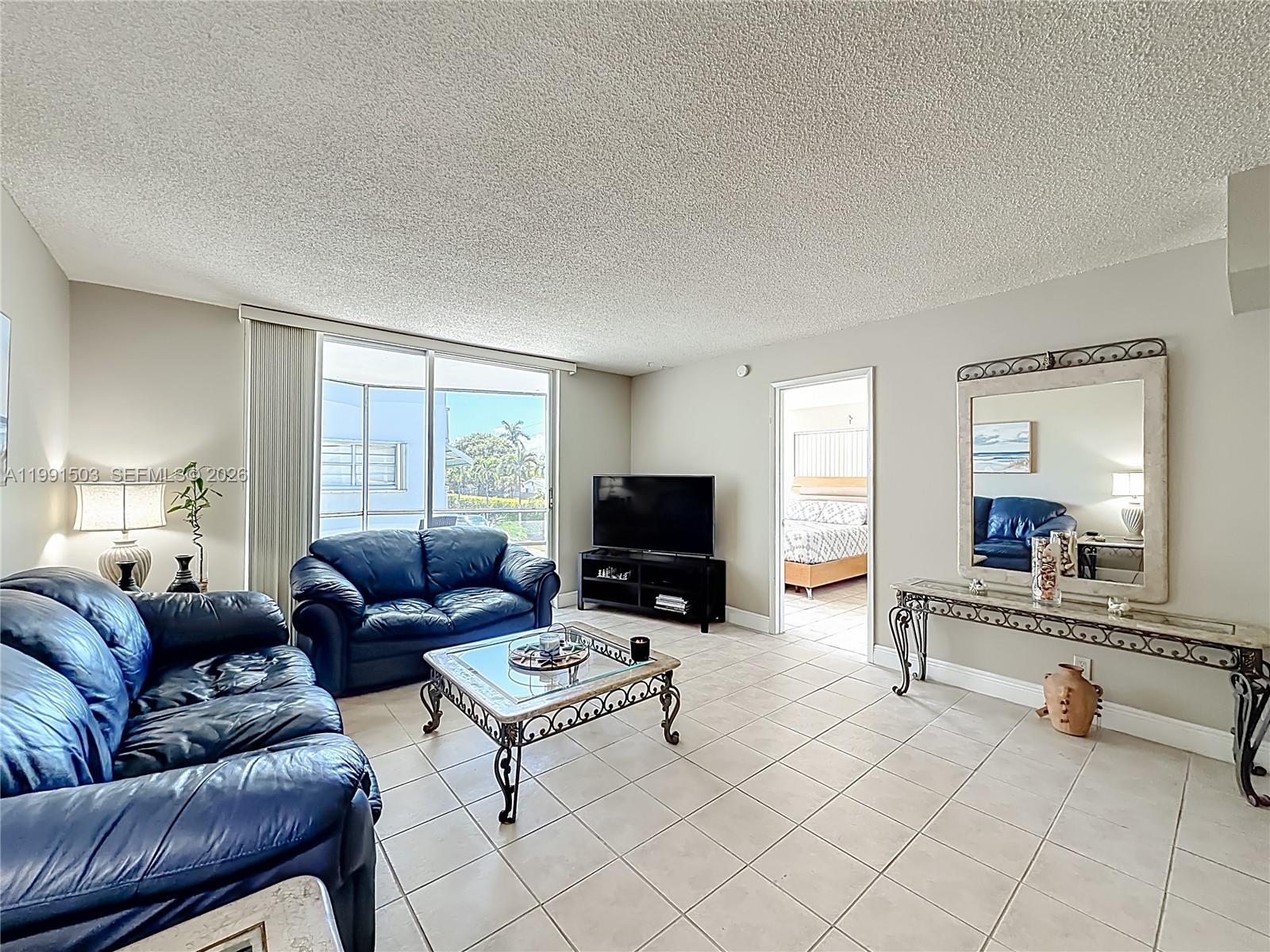 A living room features blue leather sofas, a glass-topped coffee table, and tile flooring — 400 SE 10th St # 218, Deerfield Beach FL 33441, DEERFIELD BEACH, FL