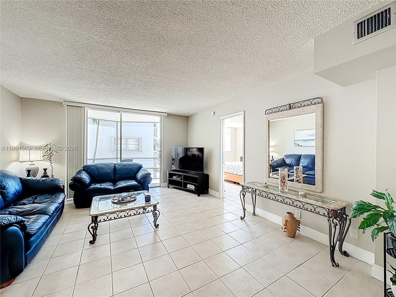 A living room features blue leather sofas, a glass coffee table, and a large wall mirror — 400 SE 10th St # 218, Deerfield Beach FL 33441, DEERFIELD BEACH, FL