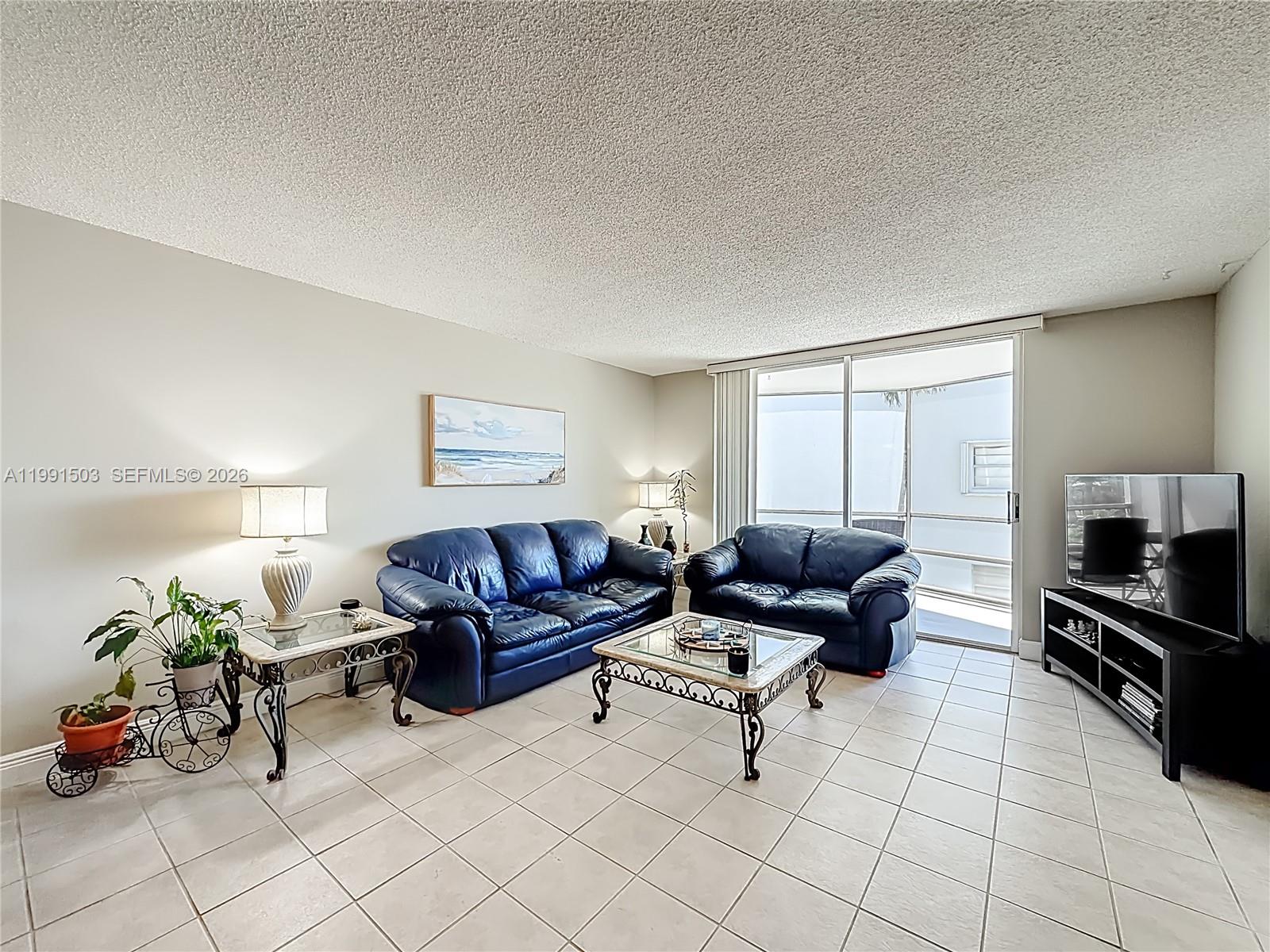 A living room features blue leather sofas, a glass coffee table, and tile flooring — 400 SE 10th St # 218, Deerfield Beach FL 33441, DEERFIELD BEACH, FL