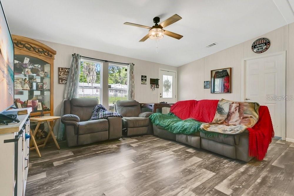 A living room features wood-look flooring, a ceiling fan, gray reclining furniture, and a television — 10787 SW 112TH AVENUE, DUNNELLON, FL
