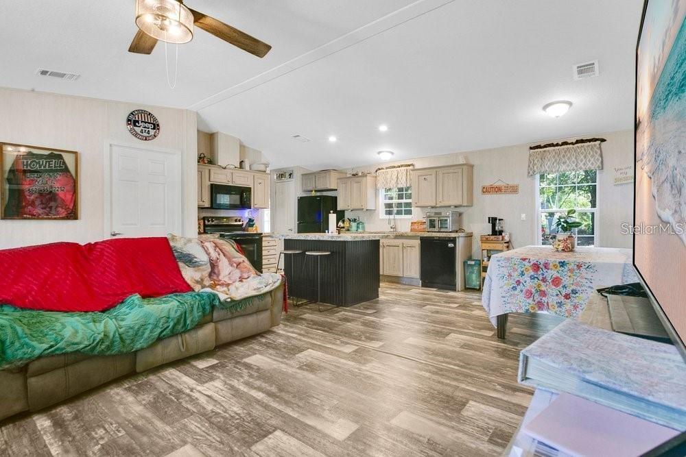 An open-concept living room and kitchen feature light wood-look flooring and a central island — 10787 SW 112TH AVENUE, DUNNELLON, FL
