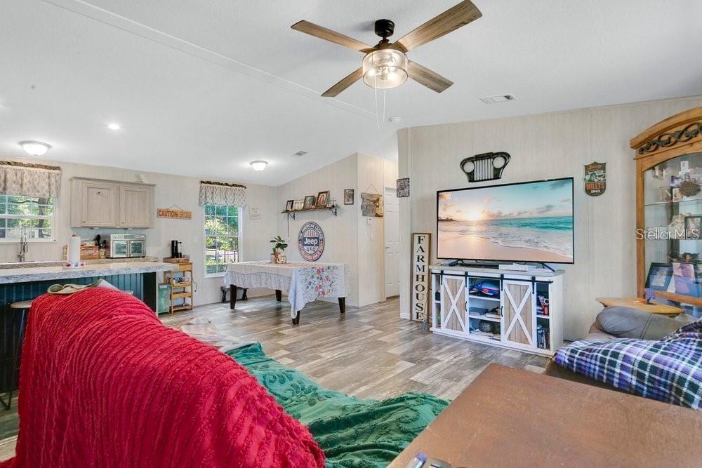 A living room and kitchen area with wood-look flooring, a ceiling fan, and farmhouse decor — 10787 SW 112TH AVENUE, DUNNELLON, FL