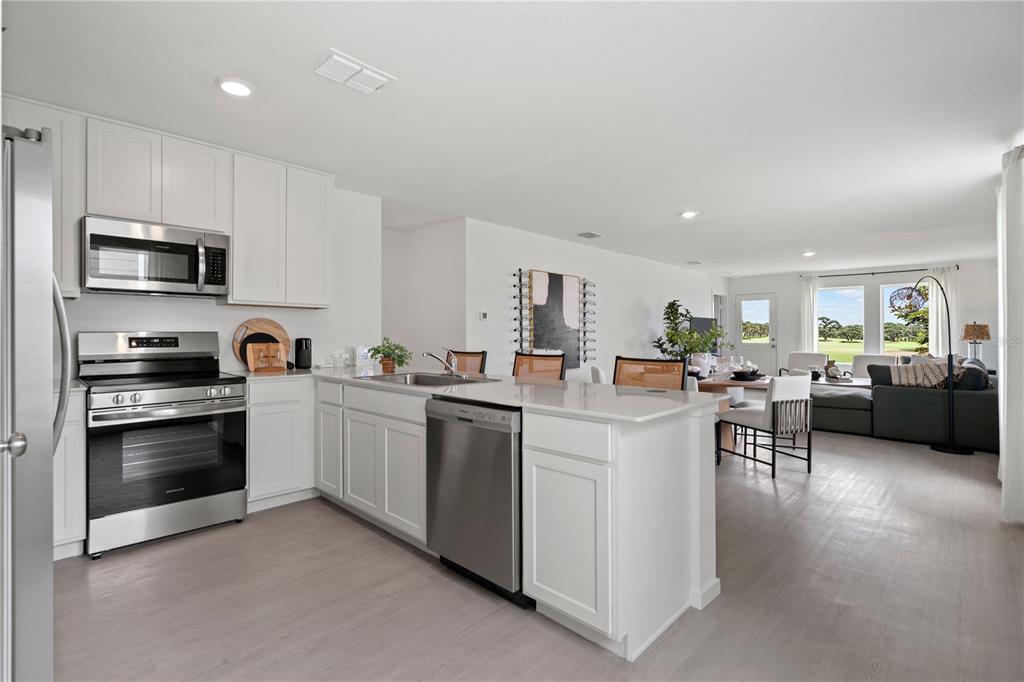 A modern kitchen with white cabinets and stainless steel appliances opens into a living area — 297 CERAMIC COURT, GROVELAND, FL