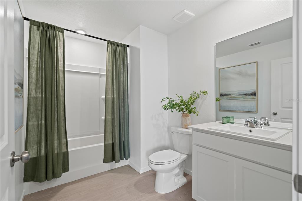 A bathroom features a white vanity, a toilet, and a bathtub with green curtains — 297 CERAMIC COURT, GROVELAND, FL