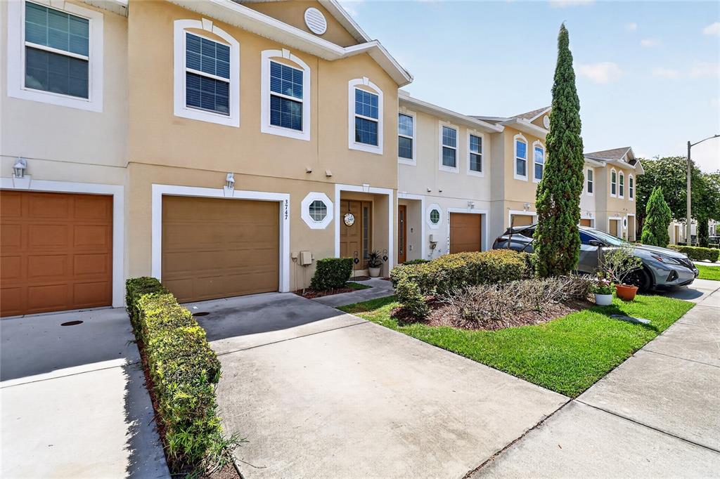 A row of tan townhouses features concrete driveways, attached garages, and small front landscaping — 3747 WOODBURY HILL LOOP, LAKELAND, FL