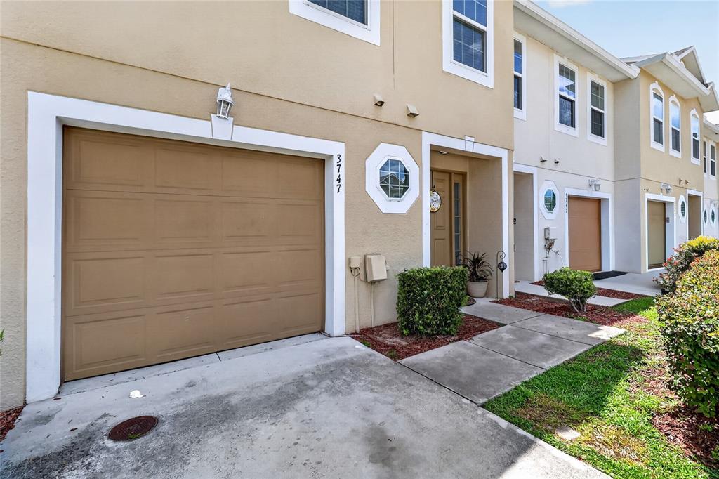 A tan two-story townhouse exterior features a single-car garage and a small front entrance — 3747 WOODBURY HILL LOOP, LAKELAND, FL