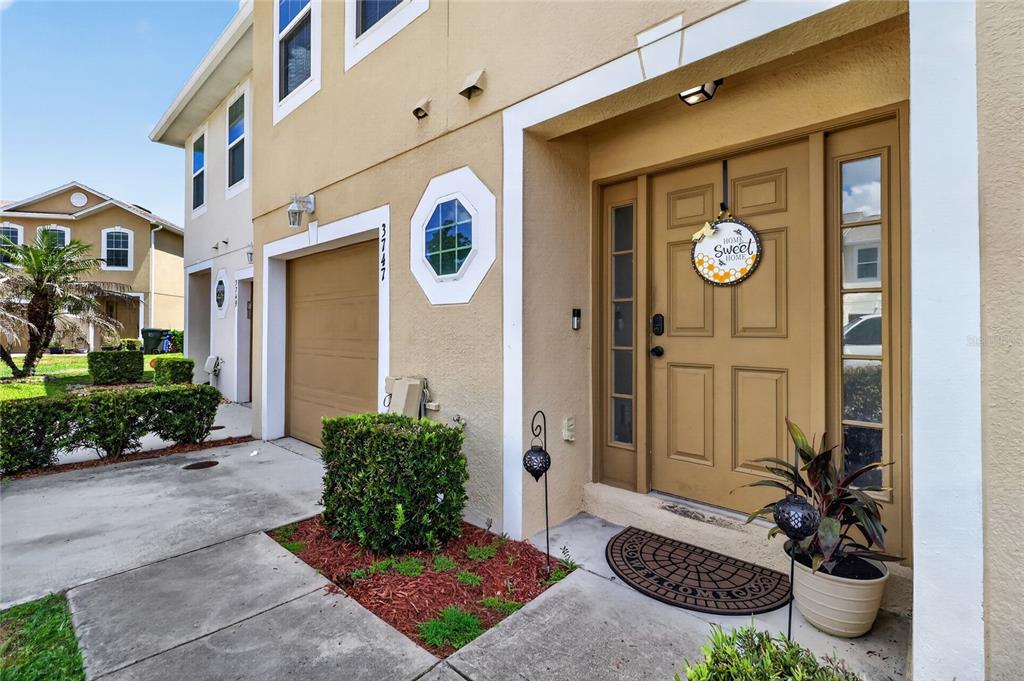A tan townhouse exterior features a garage, a front door with a wreath, and landscaping — 3747 WOODBURY HILL LOOP, LAKELAND, FL