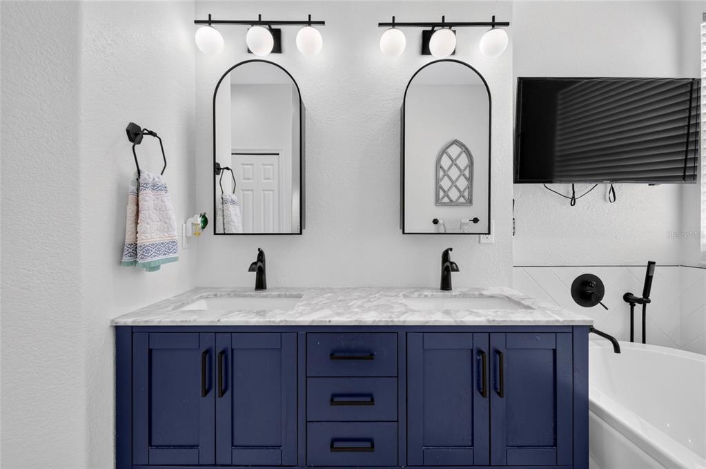 A bathroom features a double vanity with a blue cabinet, marble countertop, and arched mirrors — 353 LAKE AMBERLEIGH DRIVE, WINTER GARDEN, FL