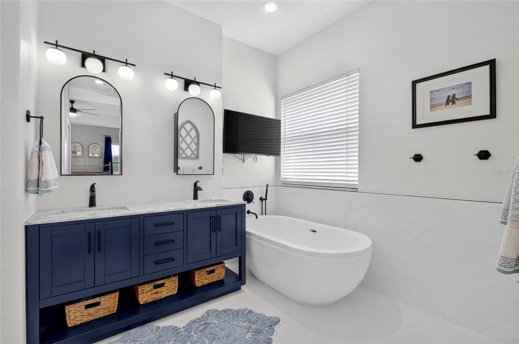 A bathroom features a navy blue double vanity, a freestanding tub, and arched mirrors — 353 LAKE AMBERLEIGH DRIVE, WINTER GARDEN, FL