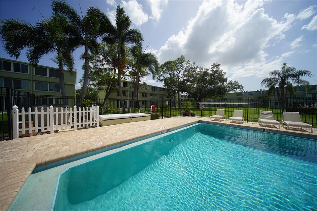 A swimming pool with a white fence and lounge chairs sits before a multi-story building — 4705 1ST STREET NE UNIT 132, ST PETERSBURG, FL
