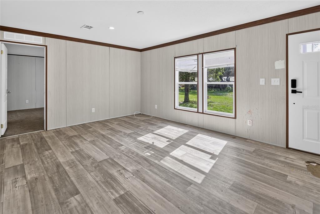 An empty room features wood-look flooring, light-colored panel walls, a window, and a white door — 17538 EVELYN COURT, SPRING HILL, FL