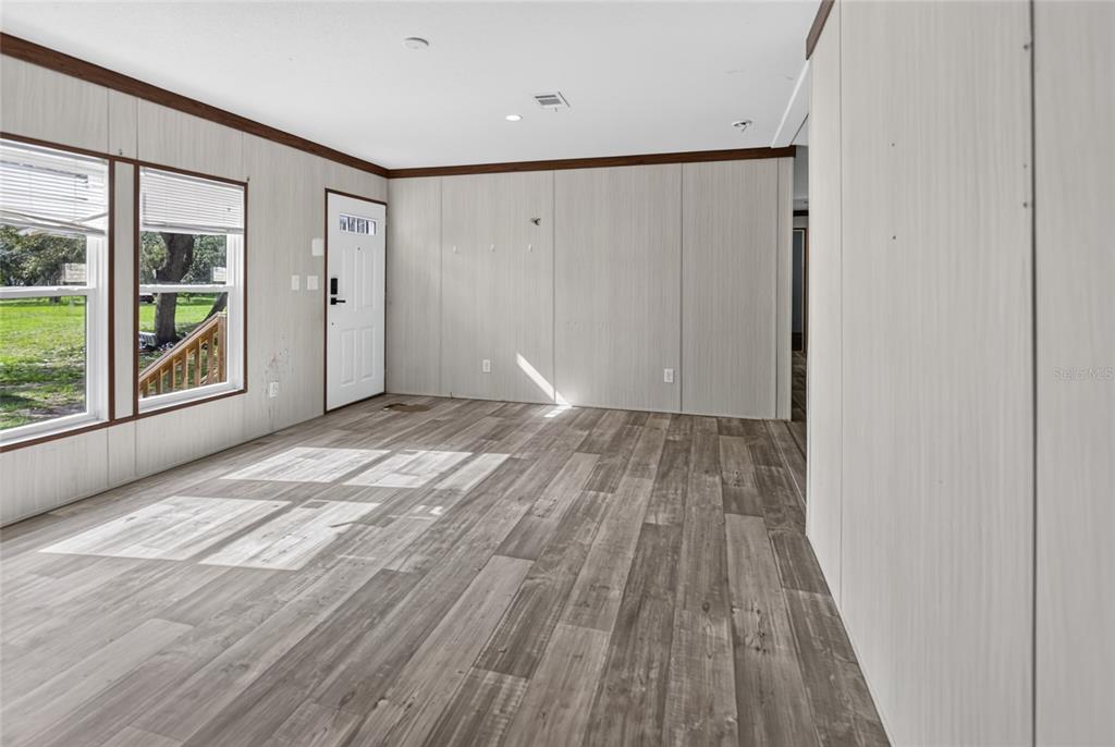 An empty room features light wood-paneled walls, gray wood-look flooring, and two windows — 17538 EVELYN COURT, SPRING HILL, FL