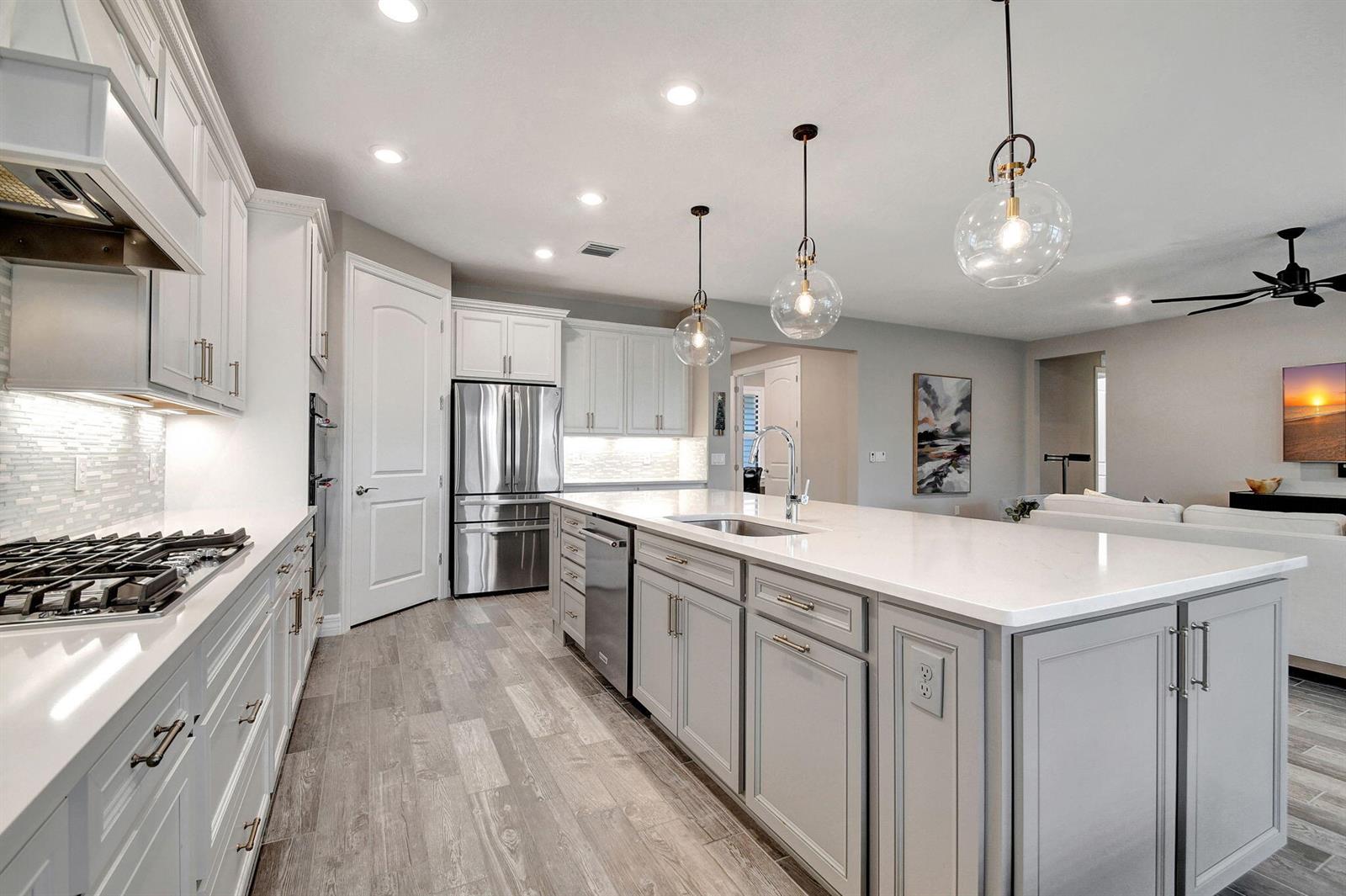 A modern kitchen features white cabinets, gray island cabinetry, stainless steel appliances, and wood-look flooring — 8433 Vaulting Drive, Lake Worth FL 33467, LAKE WORTH, FL