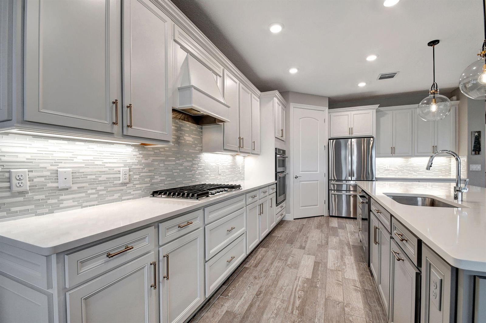A modern kitchen features white cabinetry, stainless steel appliances, quartz countertops, and a tiled backsplash — 8433 Vaulting Drive, Lake Worth FL 33467, LAKE WORTH, FL