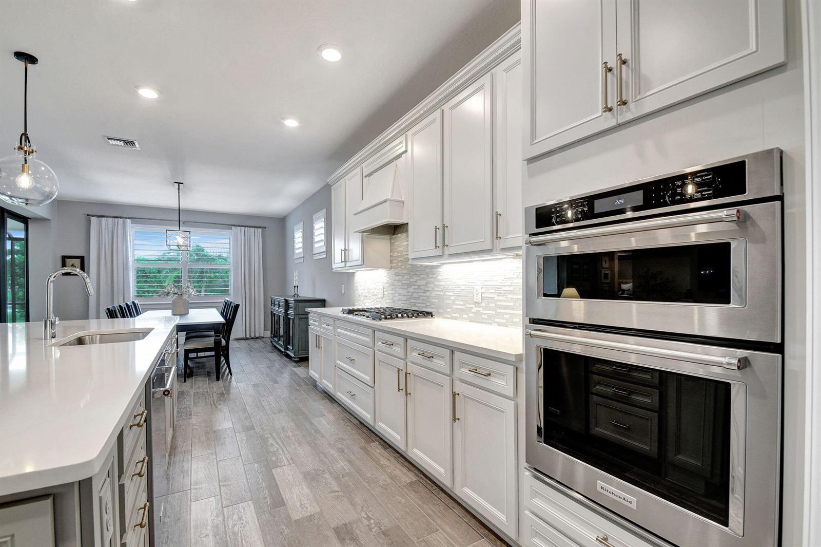 A modern kitchen features white cabinetry, stainless steel double ovens, and a large island — 8433 Vaulting Drive, Lake Worth FL 33467, LAKE WORTH, FL