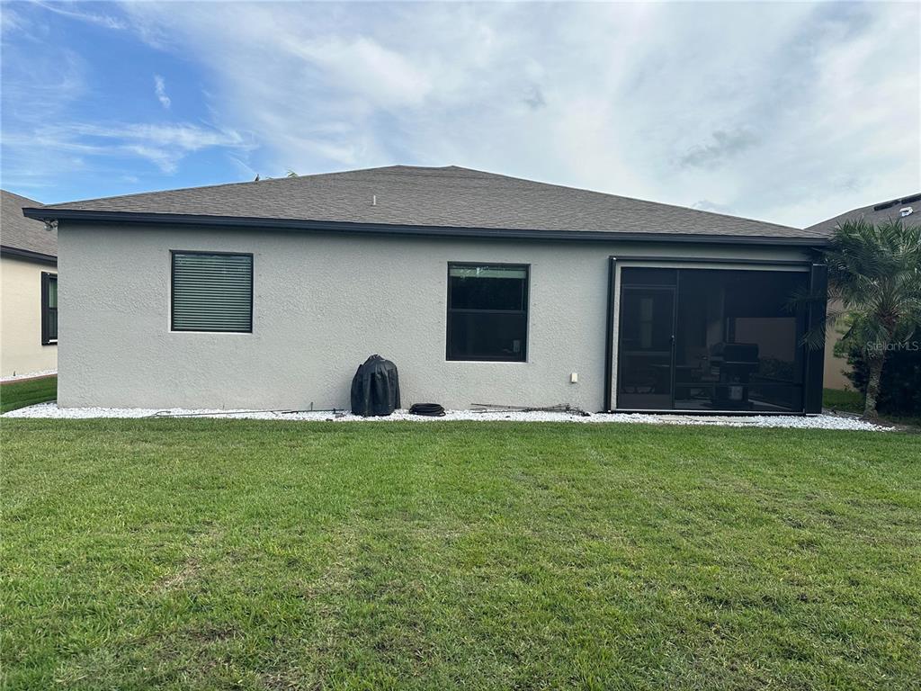 The exterior back view of a gray house features a screened-in patio and lawn — 2137 APIAN WAY, PORT CHARLOTTE, FL