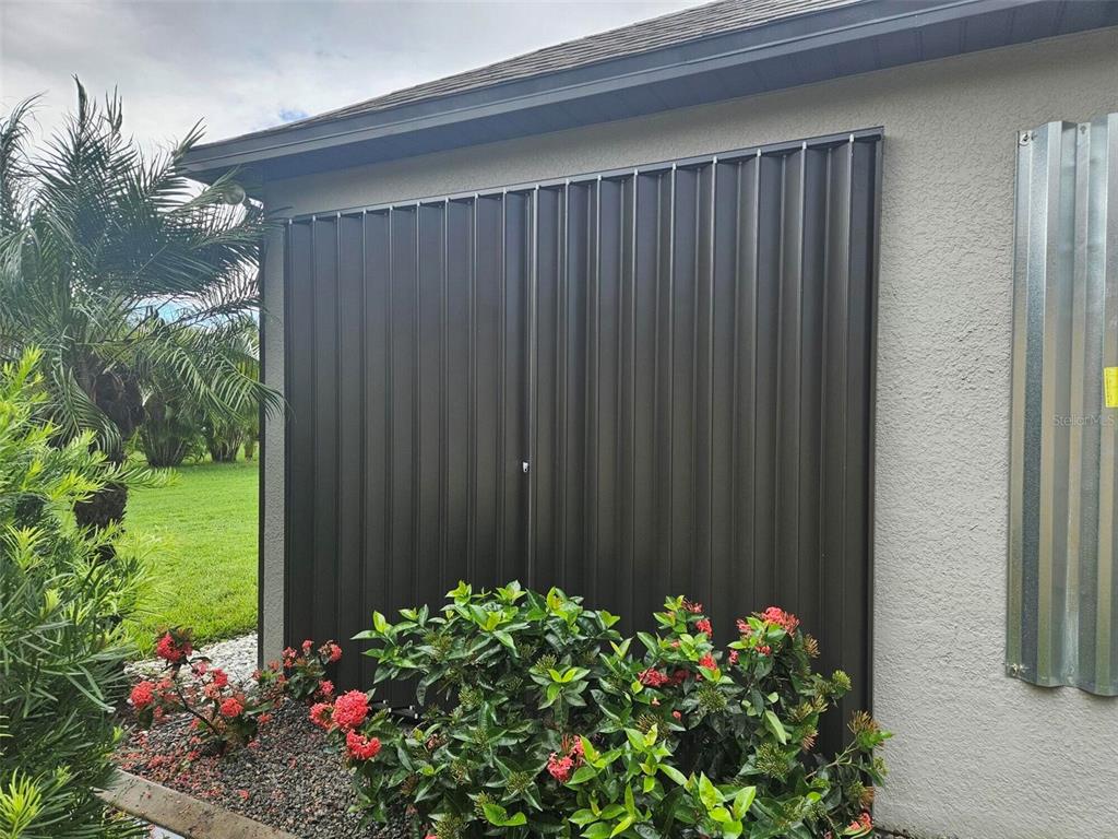 A dark brown accordion-style hurricane shutter covers a window on the exterior of a house — 2137 APIAN WAY, PORT CHARLOTTE, FL