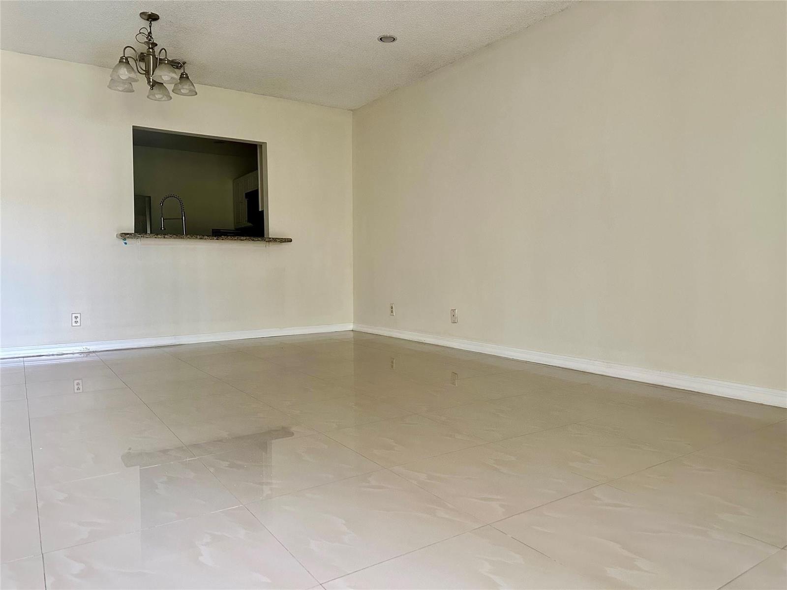 An empty room with beige tile flooring, a pass-through window to the kitchen, and chandelier — 22415 SW 61st Way # 202, Boca Raton FL 33428, BOCA RATON, FL