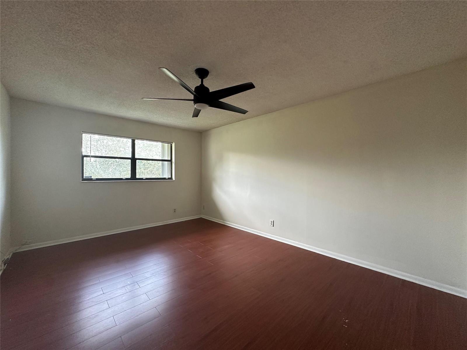 An empty room features dark wood-look flooring, white walls, and a black ceiling fan — 22415 SW 61st Way # 202, Boca Raton FL 33428, BOCA RATON, FL