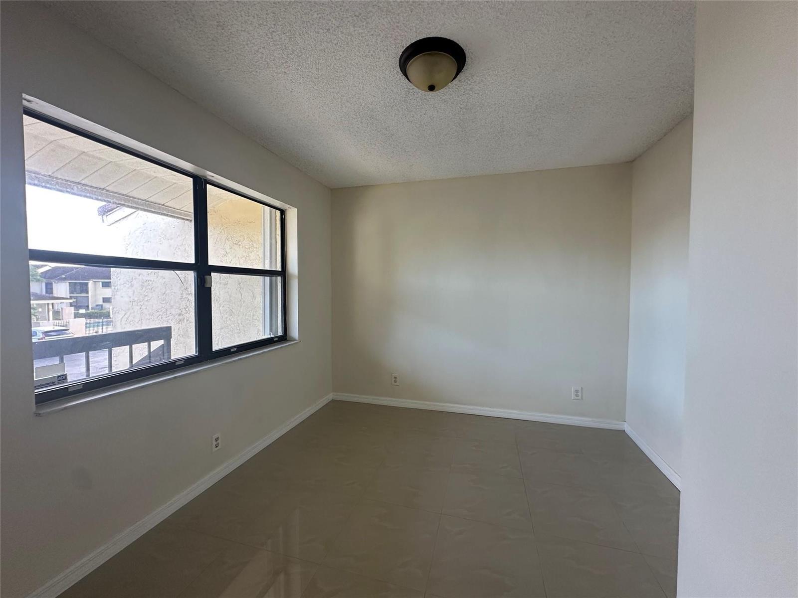 An empty room features beige walls, large windows, and light-colored tile flooring — 22415 SW 61st Way # 202, Boca Raton FL 33428, BOCA RATON, FL