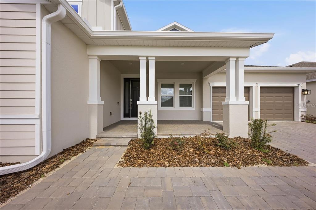 A paved walkway leads to the covered front porch and entrance of a suburban home — 12893 HARVEST RAIN AVENUE, WINTER GARDEN, FL