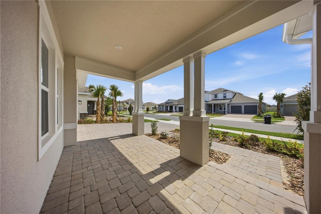 A covered front porch with paver flooring overlooks a suburban street with neighboring houses — 12893 HARVEST RAIN AVENUE, WINTER GARDEN, FL