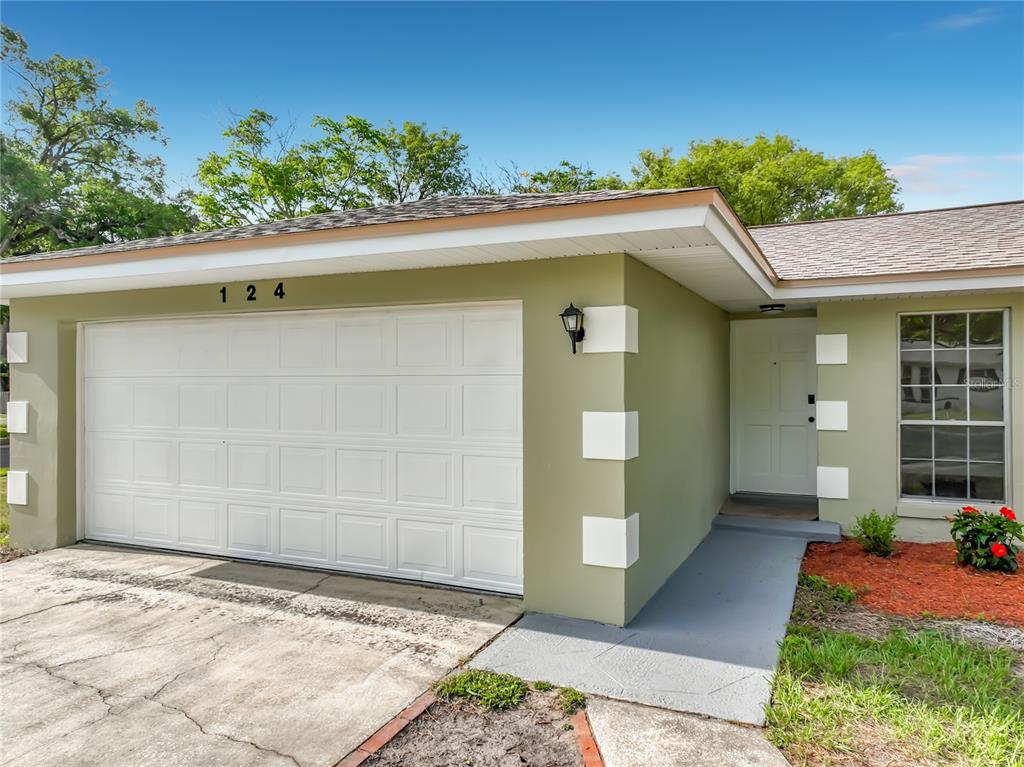 A single-story house with a green exterior, white garage door, and a front entrance walkway — 124 HOLLYHOCK DRIVE, ALTAMONTE SPRINGS, FL