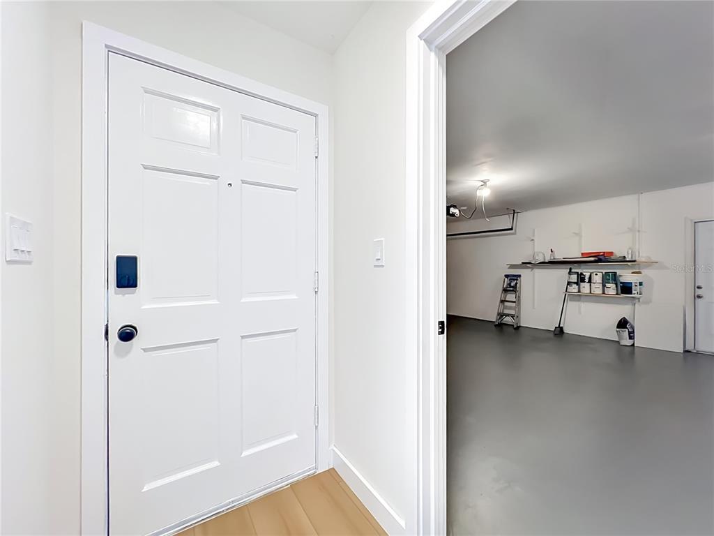 A white door with a smart lock opens into a garage with grey flooring — 124 HOLLYHOCK DRIVE, ALTAMONTE SPRINGS, FL