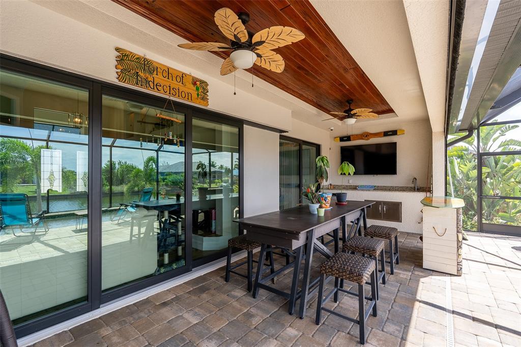 A covered outdoor patio features a dining table, ceiling fans, a television, and sliding glass doors — 15252 CHINOOK WAY, PORT CHARLOTTE, FL