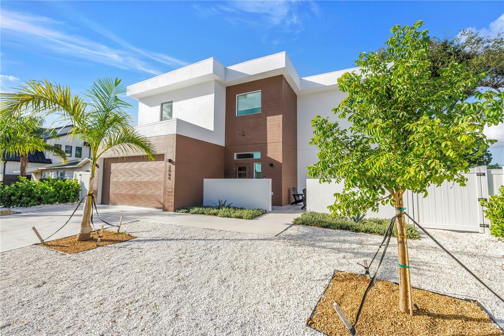 A modern two-story house with a brown and white exterior, gravel yard, and two young trees — 2065 GOLDENROD STREET, SARASOTA, FL