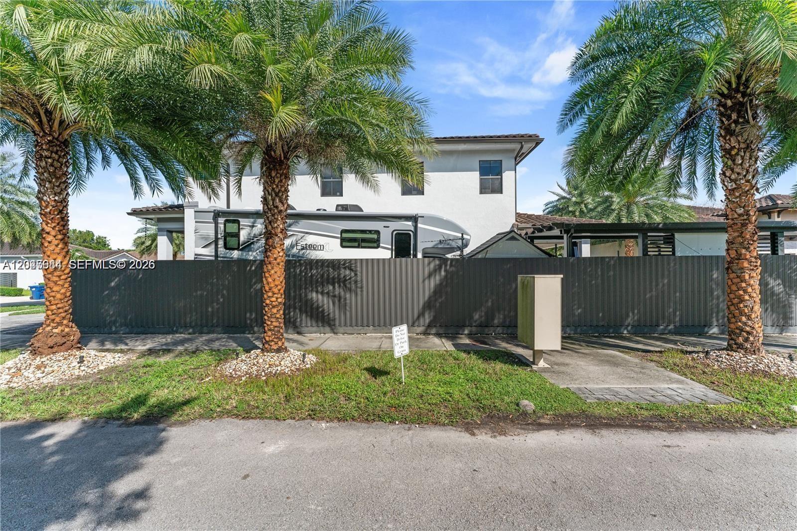 A two-story house is visible behind a tall gray fence and two palm trees — 14856 SW 27th Ter, Miami FL 33185, MIAMI, FL