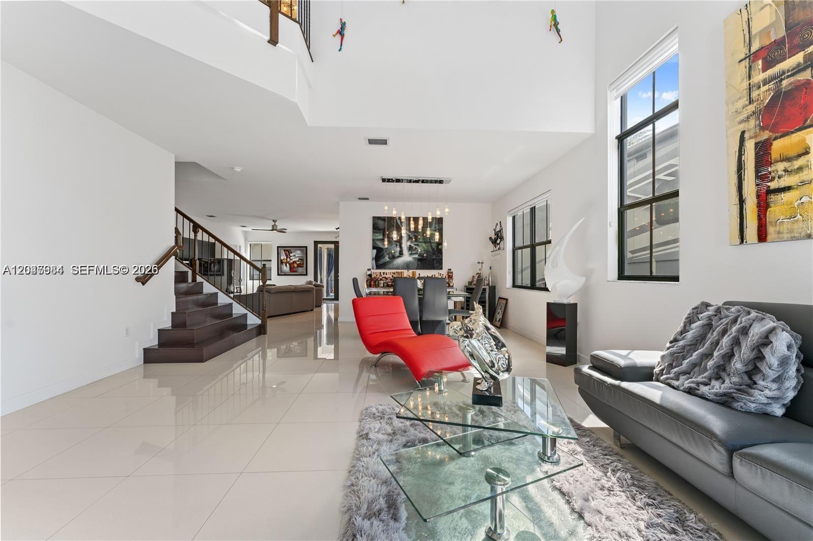 A modern living room features white walls, tile floors, a red chaise, and a staircase — 14856 SW 27th Ter, Miami FL 33185, MIAMI, FL