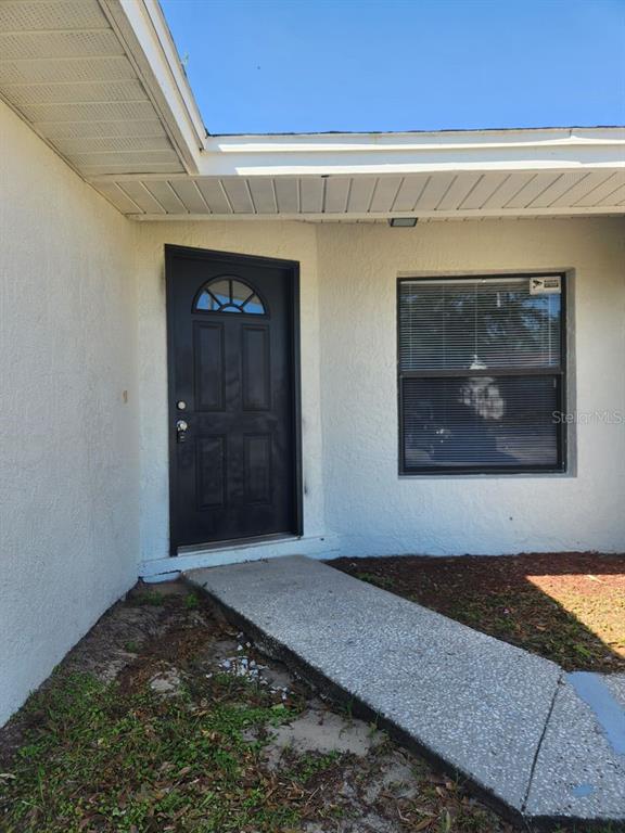 A black front door and a window are set into the white stucco exterior wall — 661 N DELMONTE COURT, KISSIMMEE, FL