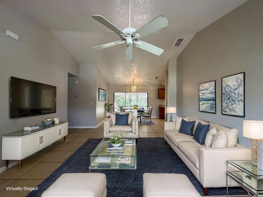 A living room with a ceiling fan, beige sofa, armchair, and a glass coffee table — 661 N DELMONTE COURT, KISSIMMEE, FL