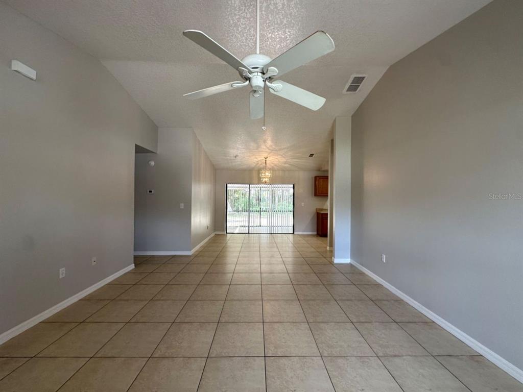 A spacious living room features vaulted ceilings, a ceiling fan, and light-colored tile flooring — 661 N DELMONTE COURT, KISSIMMEE, FL