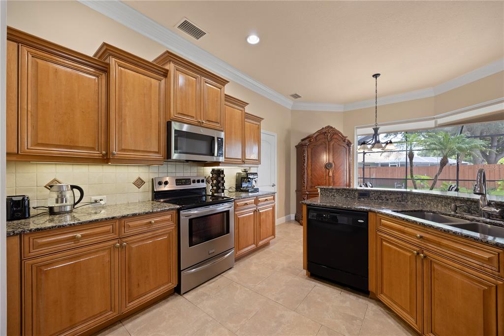 A kitchen features wood cabinets, granite countertops, stainless steel appliances, and a black dishwasher — 1276 RAMROD STREET, NORTH PORT, FL
