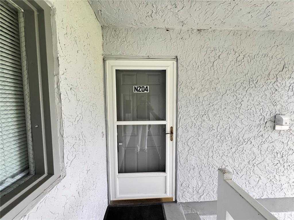 A white storm door with the number N204 is set into a textured white exterior wall — 572 SE FAIRWAYS LANE UNIT N204, OCALA, FL