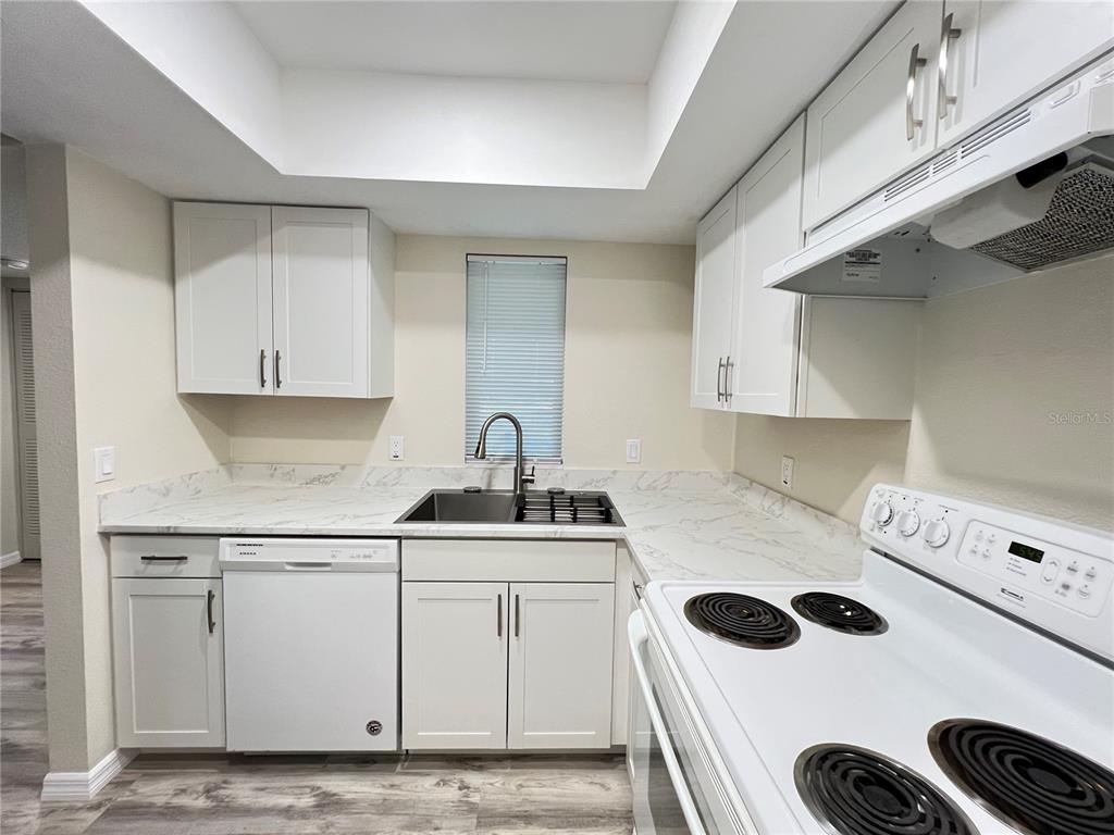 A kitchen features white cabinets, marble-look countertops, a stainless steel sink, and white appliances — 572 SE FAIRWAYS LANE UNIT N204, OCALA, FL