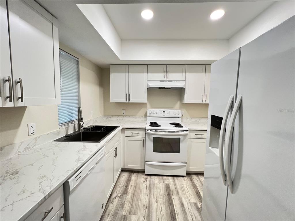 A kitchen with white cabinets, marble-patterned countertops, a white stove, and a white refrigerator — 572 SE FAIRWAYS LANE UNIT N204, OCALA, FL