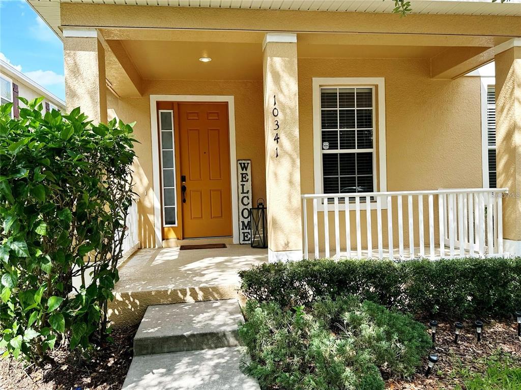 The exterior of a house features a tan porch, a yellow front door, and white railings — 10341 LAKE DISTRICT LANE UNIT 55B, ORLANDO, FL