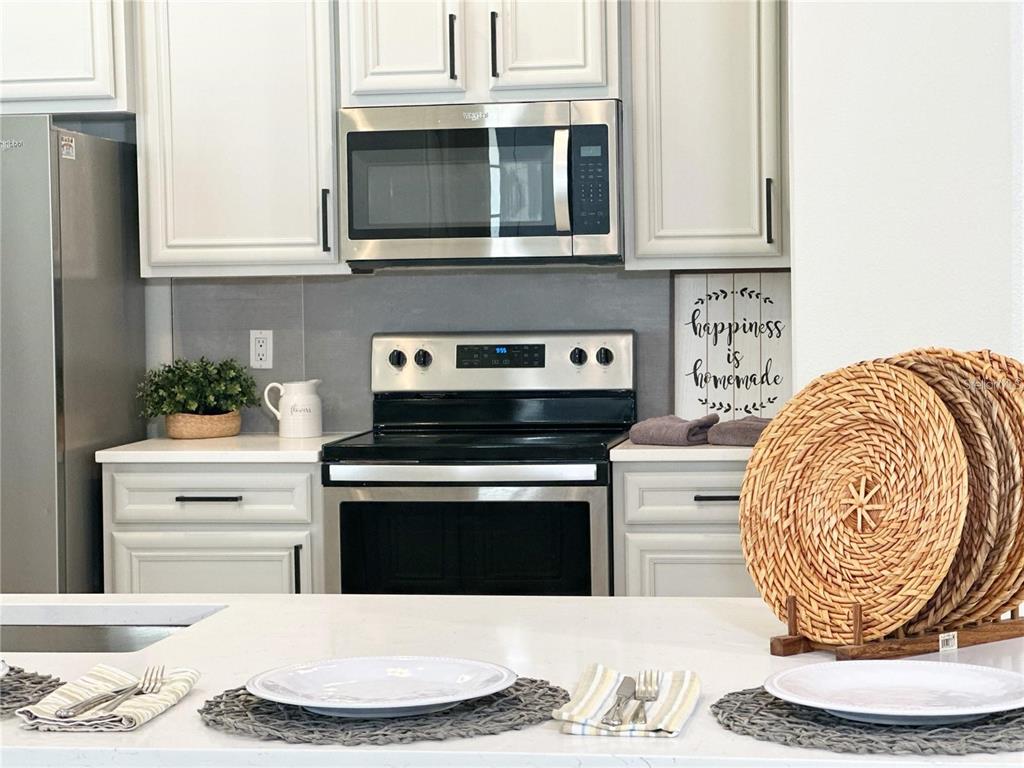 A kitchen features white cabinets, stainless steel appliances, a gray backsplash, and a white island — 10341 LAKE DISTRICT LANE UNIT 55B, ORLANDO, FL