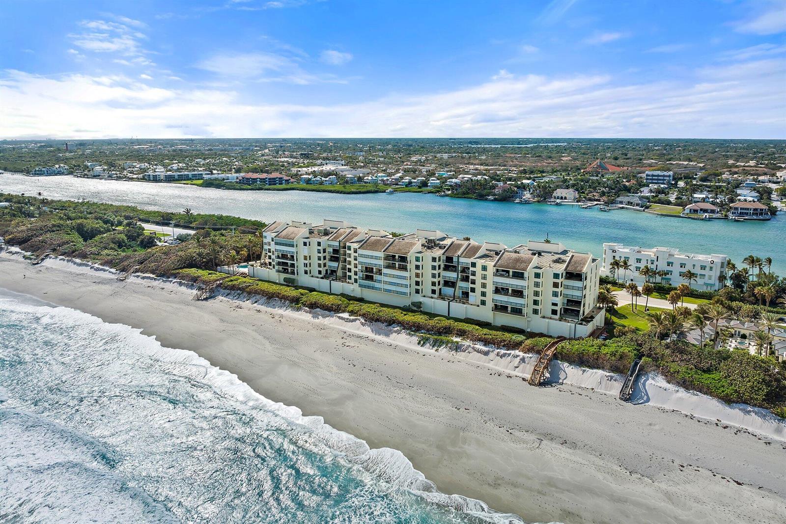 An aerial view shows a multi-story residential building situated between a sandy beach and a waterway — 19670 Beach Road # C513, Jupiter FL 33469, JUPITER, FL