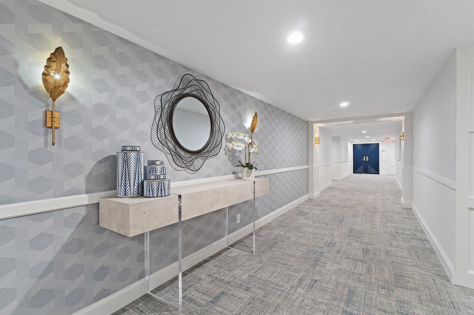 A hallway features patterned wallpaper, a floating console table, a decorative mirror, and wall sconces — 19670 Beach Road # C513, Jupiter FL 33469, JUPITER, FL