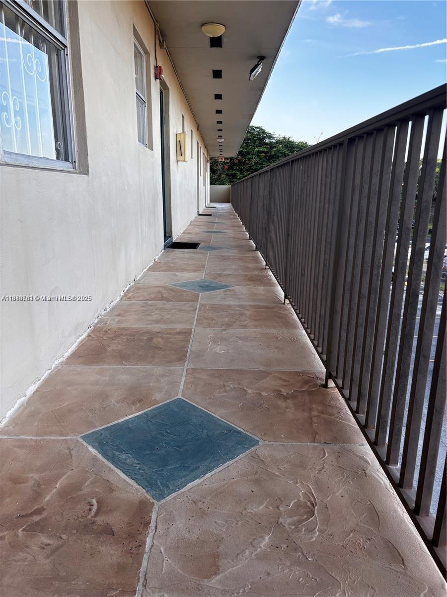 An outdoor apartment walkway features brown tiled flooring with blue diamond-shaped accents and metal railings — 7505 SW 82nd St # 318, Miami FL 33143, MIAMI, FL